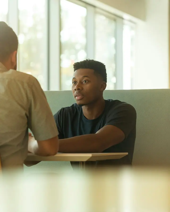 Two people in a one-on-one conversation at a table in warm afternoon light