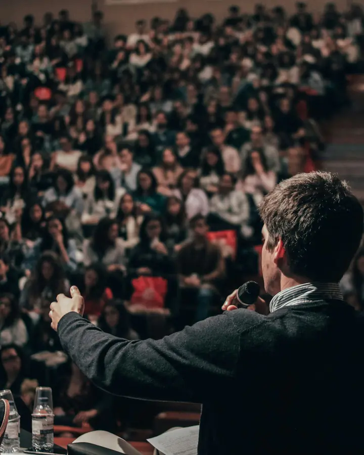 A speaker addressing a full auditorium, seen from behind